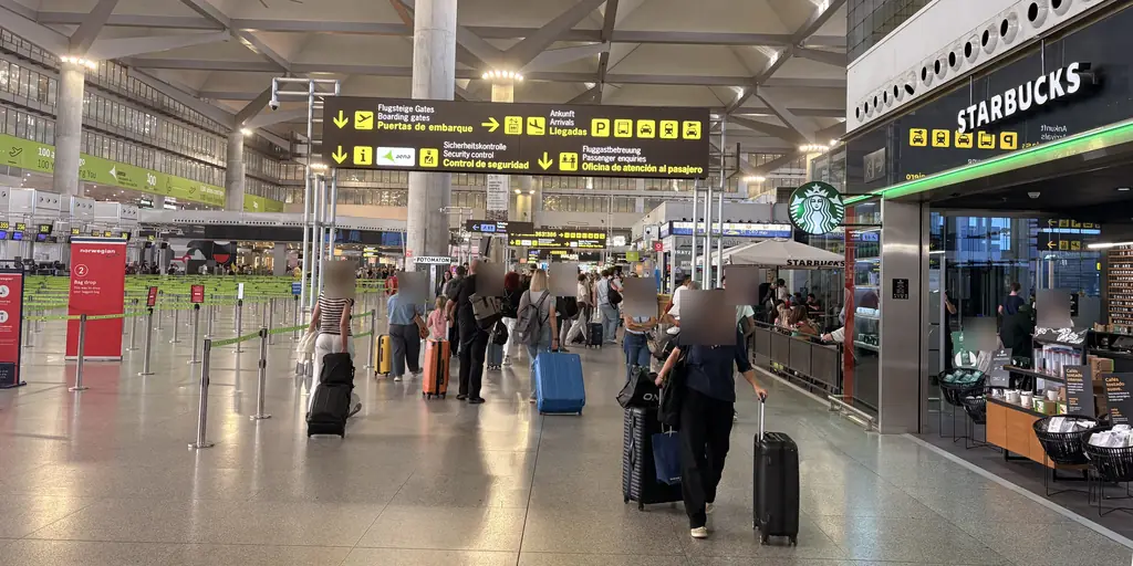 Passengers with suitcases walking through the Málaga Airport check-in hall towards the security control signs