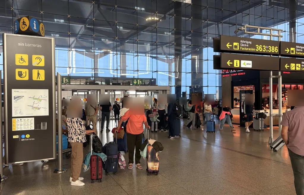 Málaga Airport terminal entrance with a Sin Barreras information column and signs to check-in desks 363 to 386